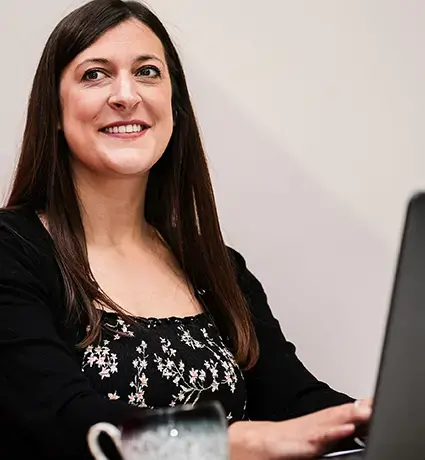 A woman sitting on a red bench, typing on a laptop resting on a white table.