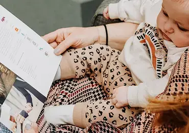 A baby is sitting on a woman's lap and they are browsing a law brochure.