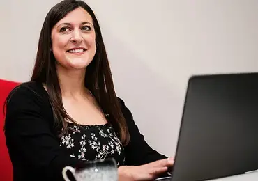 A woman sitting on a red bench, typing on a laptop resting on a white table.